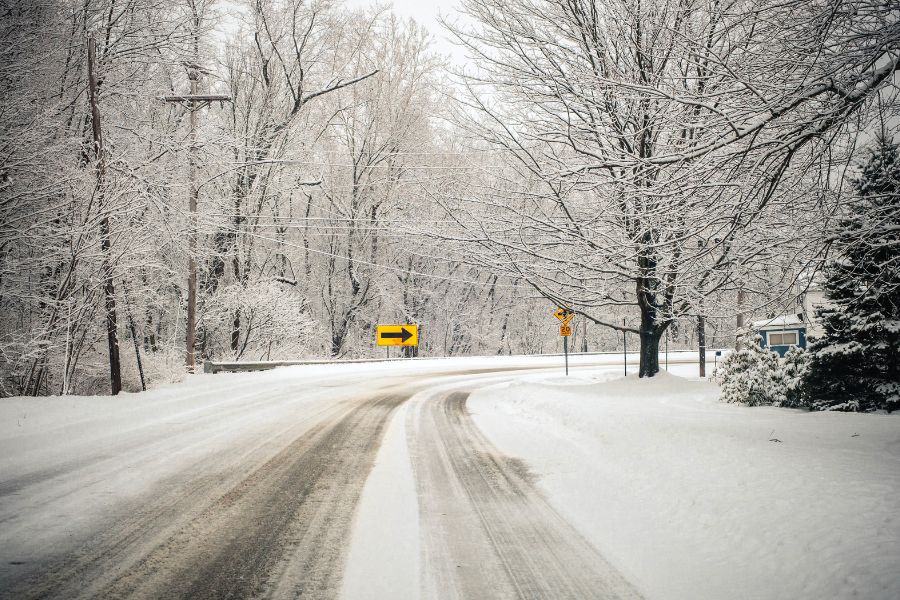 Snow-covered road with icy conditions and a curve sign, representing factors in school district snow day policies.