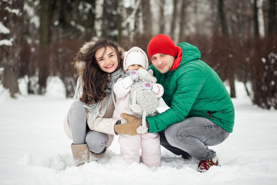 Smiling parents with their child outdoors in the snow, representing family preparation for unexpected snow days.